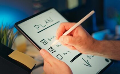 Person using a digital tablet and stylus to plan and organize tasks in an office setting.